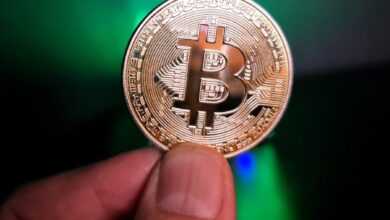 a hand holding a bit coin in front of a green light