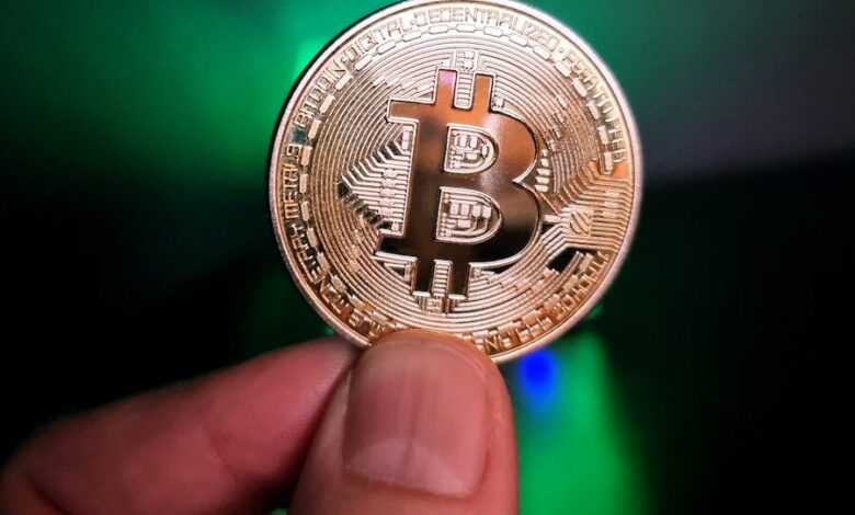 a hand holding a bit coin in front of a green light